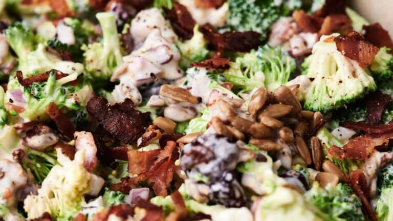 A close-up of a broccoli salad with bacon, sunflower seeds, red onions, and a creamy dressing.