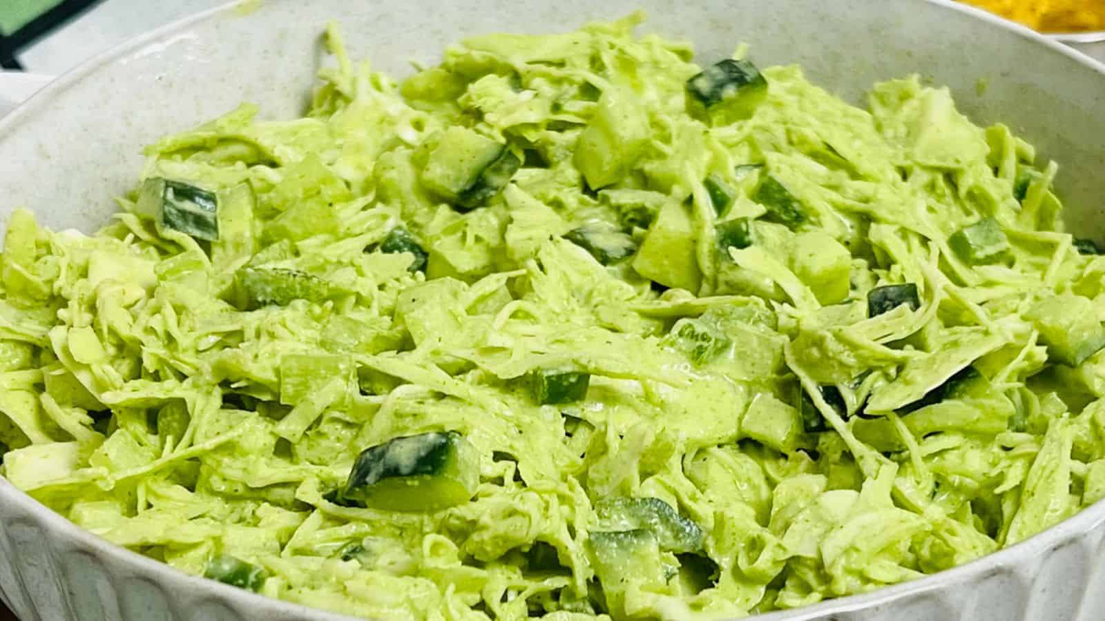 Cabbage salad in a white bowl with chips in the background.