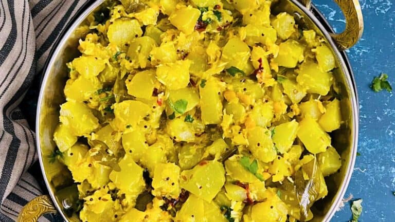 A bowl of cooked yellow squash garnished with herbs and spices, with a striped cloth napkin beside it.