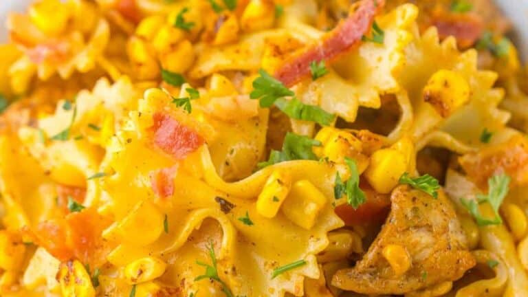 Close-up of a pasta dish garnished with corn, bacon, and herbs, featuring a creamy orange sauce.