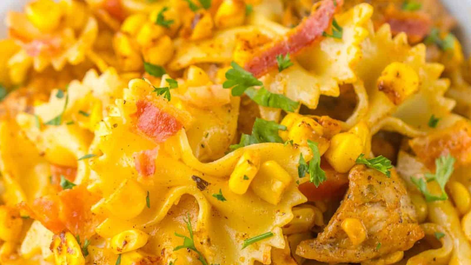 Close-up of a pasta dish with corn, bacon, and herbs, seasoned with a creamy yellow sauce.