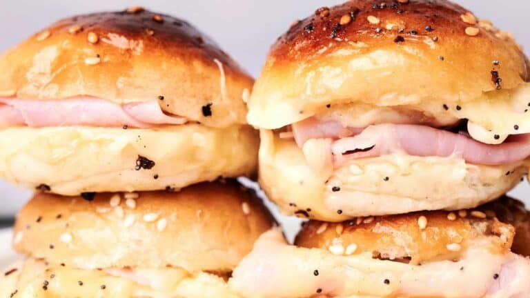 Four ham and cheese sliders on sesame seed buns stacked on top of each other.