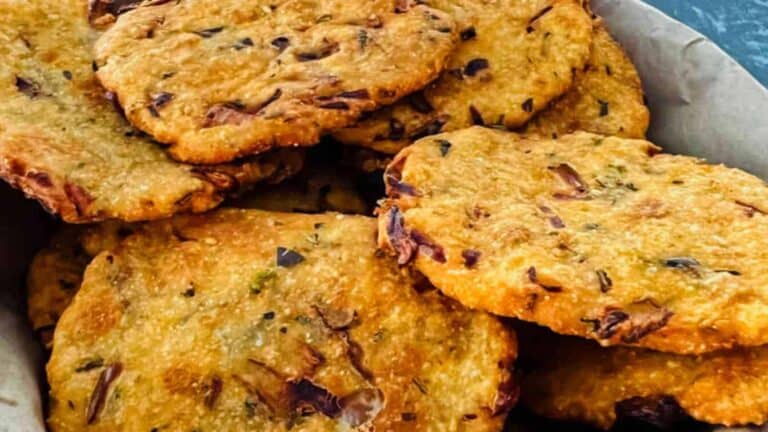 A basket of crispy, round fried snacks with visible herbs and small pieces of onion.