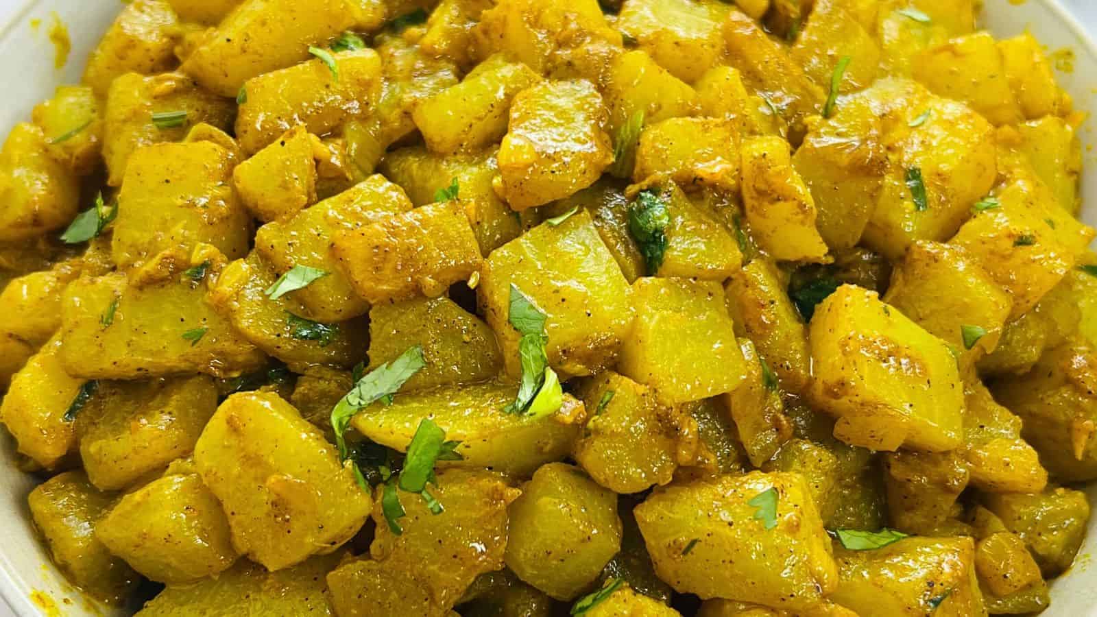 Close-up of a bowl filled with diced potatoes cooked with turmeric, garnished with chopped cilantro.