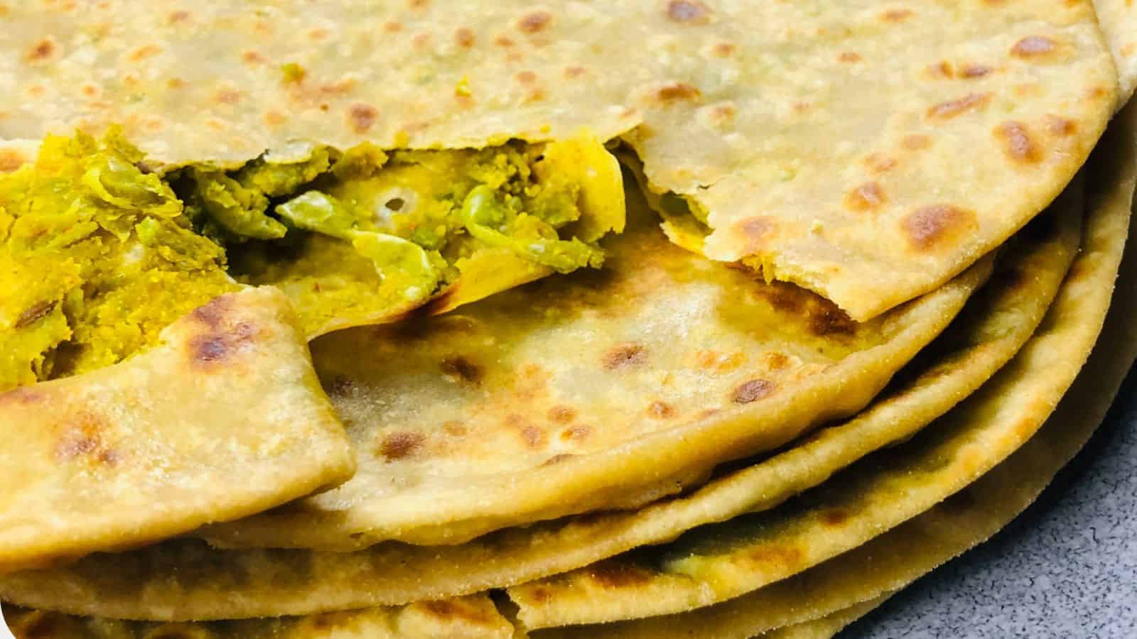 Close-up of a stack of Peas Paratha, one partly unfolded to reveal a filling of spicy cauliflower mixture.