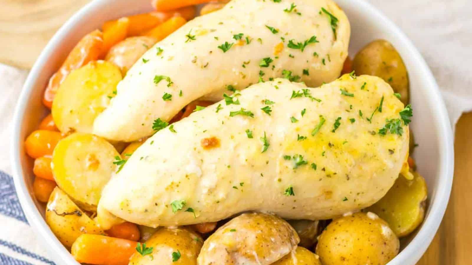 A dish of seasoned chicken breasts garnished with parsley, surrounded by carrots and potatoes in a bowl.