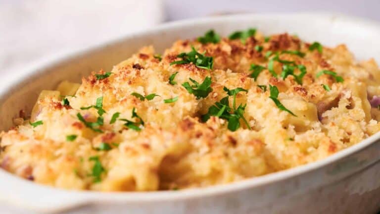 A close-up of a baked macaroni and cheese dish, topped with a golden breadcrumb crust and garnished with chopped parsley, served in a white oval dish.