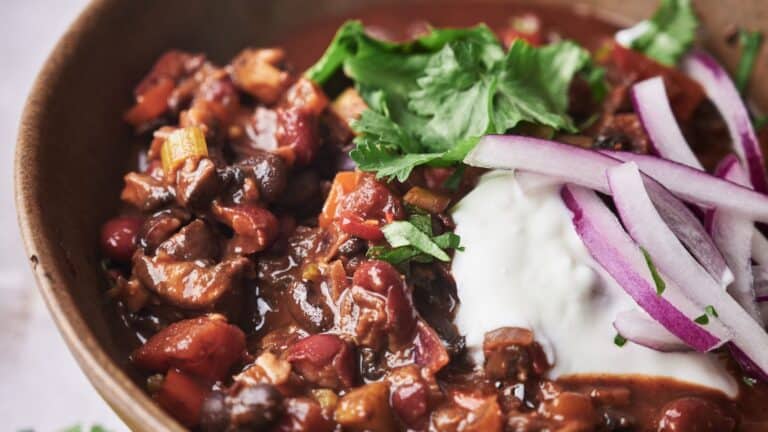 Close-up of a bowl of chili topped with chopped cilantro, red onion slices, and a dollop of sour cream.