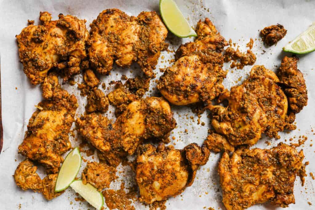 Close-up of seasoned and cooked chicken pieces arranged on parchment paper with lime wedges.