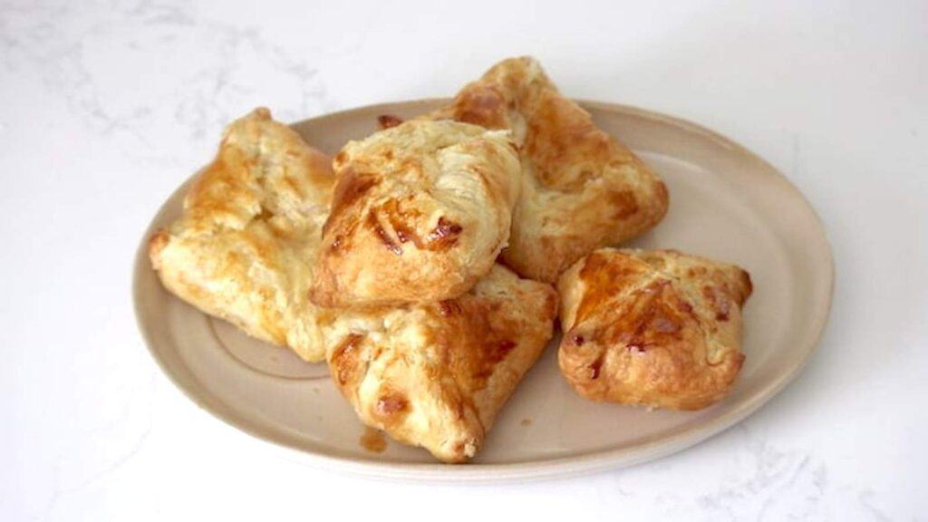 A plate with puff pastry cheese pockets on a white marble background.