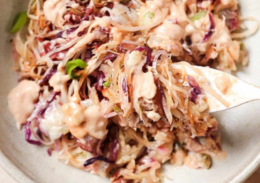 A close-up of a Reuben bowl with red and white cabbage, mixed and topped with a pink dressing, served on a light beige plate.