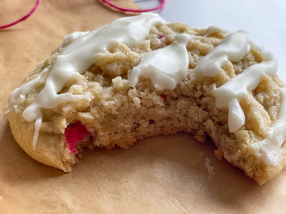 A half-eaten cookie with pink filling and white icing on a light surface.