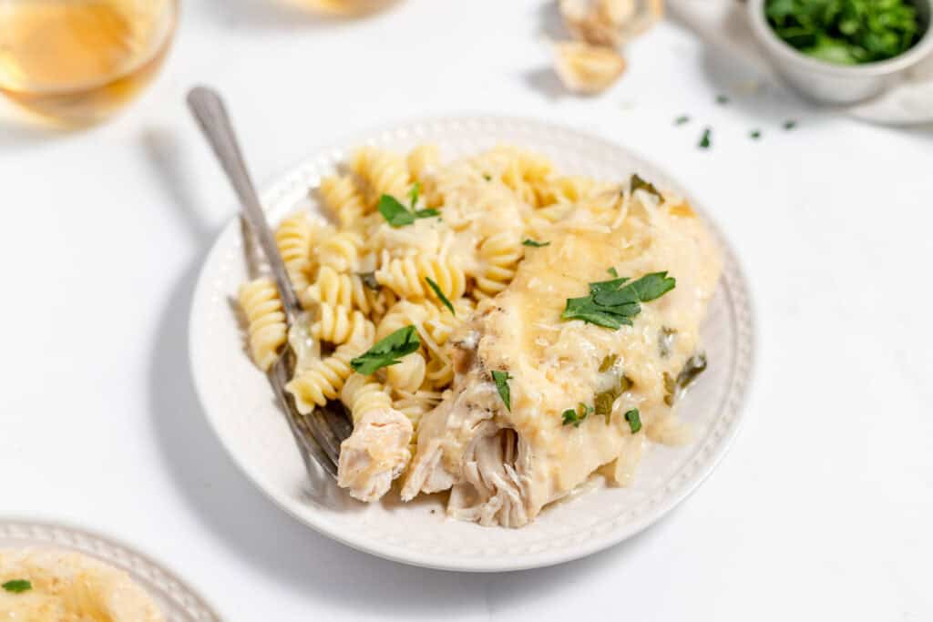A plate of creamy chicken pasta topped with parmesan and herbs, accompanied by a fork, on a white background.