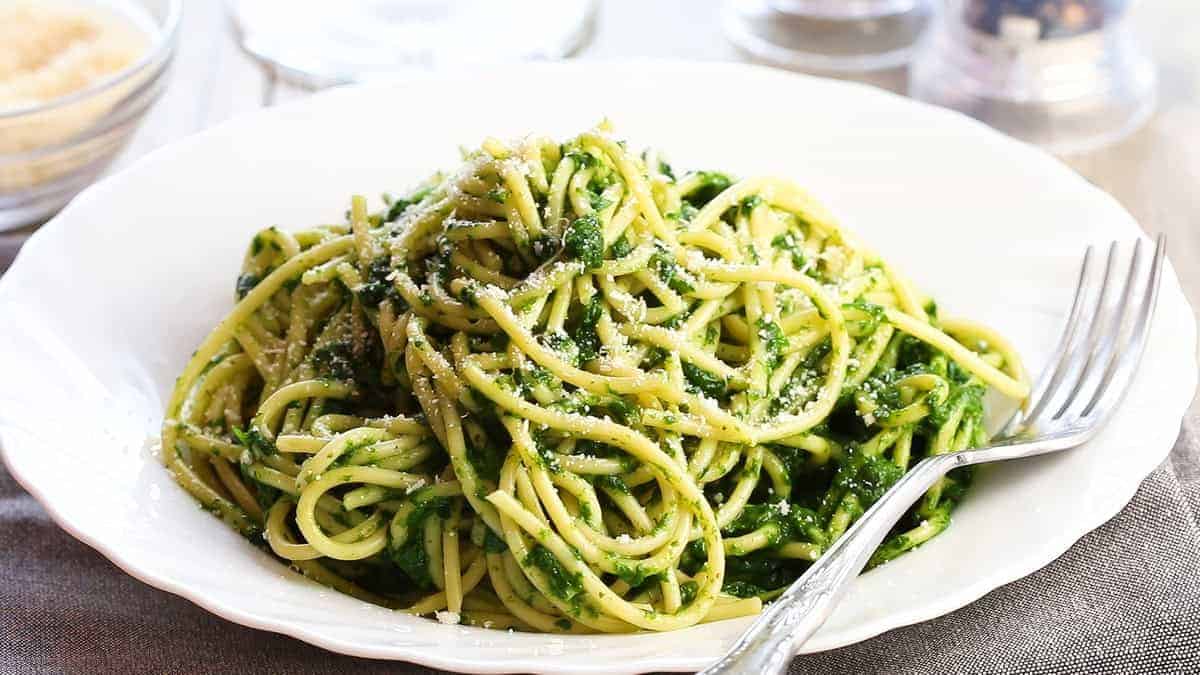 A bowl of Spaghetti with Spinach Sauce with a fork next to it on the plate.