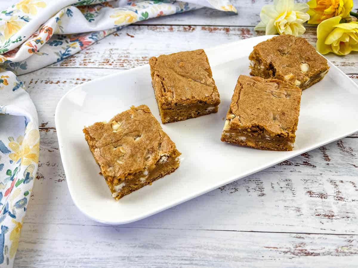 A white plate with four square pieces of Speculoos White Chocolate Blondies bars.