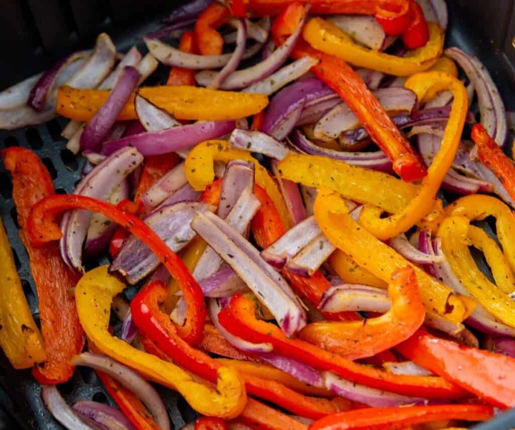 Mixed bell peppers and red onions sautéed in a pan, featuring vibrant red, orange, yellow, and purple colors.