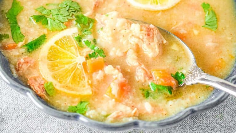 A bowl of lemon rice soup garnished with parsley, featuring slices of lemon and visible chunks of chicken and vegetables.