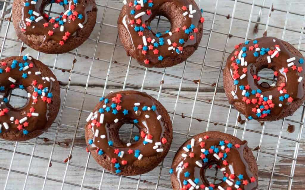 Chocolate-glazed donuts on a cooling rack, decorated with red, white, and blue sprinkles.