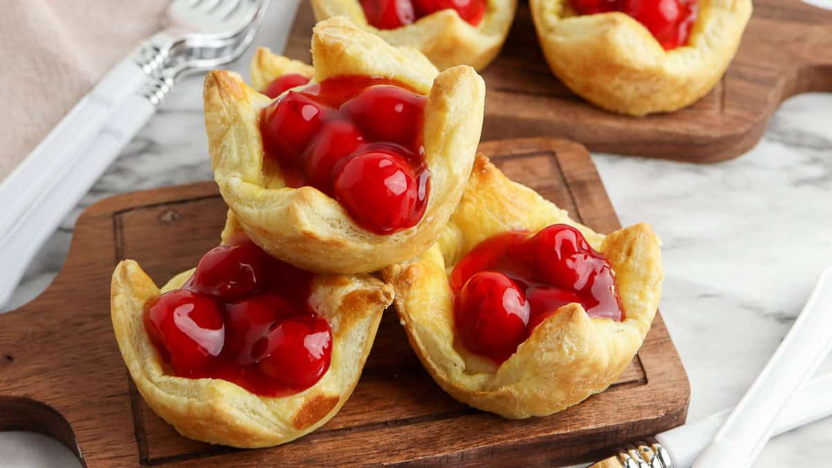 Cherry pastries arranged on a wooden board, featuring flaky golden crusts filled with vibrant red cherries.