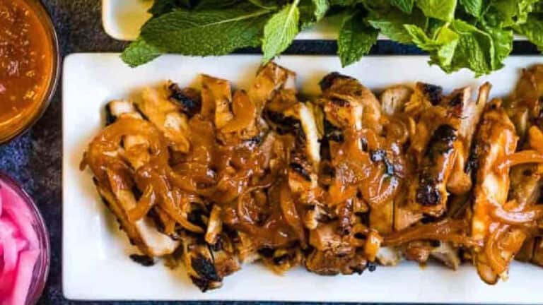 Grilled chicken topped with caramelized onions and served with fresh herbs and sauce on a white rectangular plate.