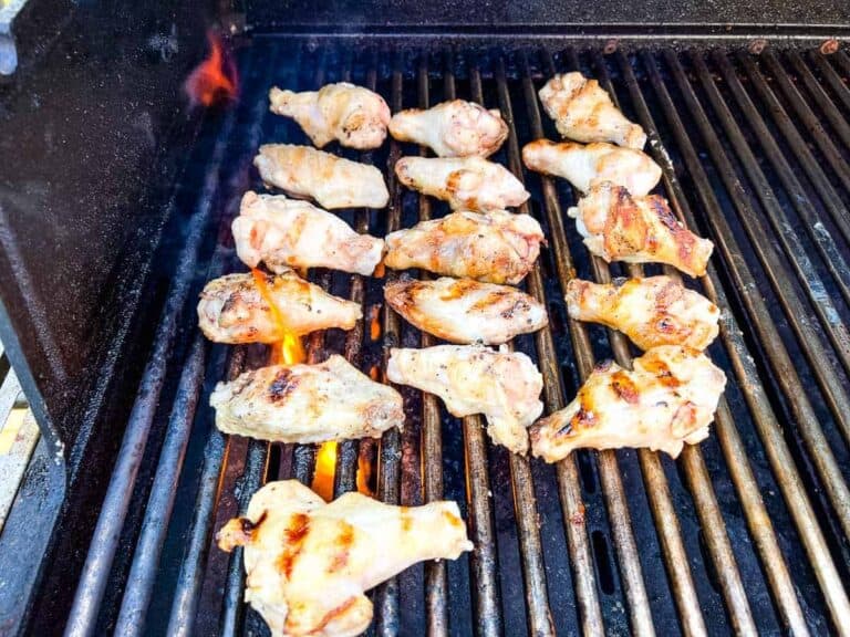 Chicken drumsticks grilling on a barbecue with visible flames.