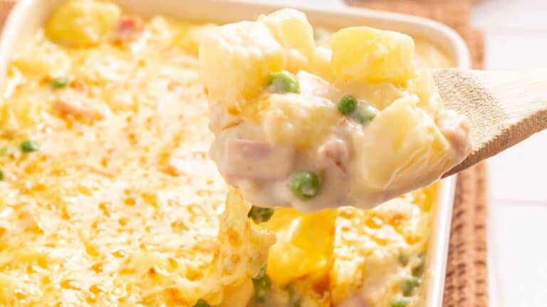A creamy tuna noodle casserole with peas scooped up with a wooden spoon, bubbly cheese crust visible in the background.