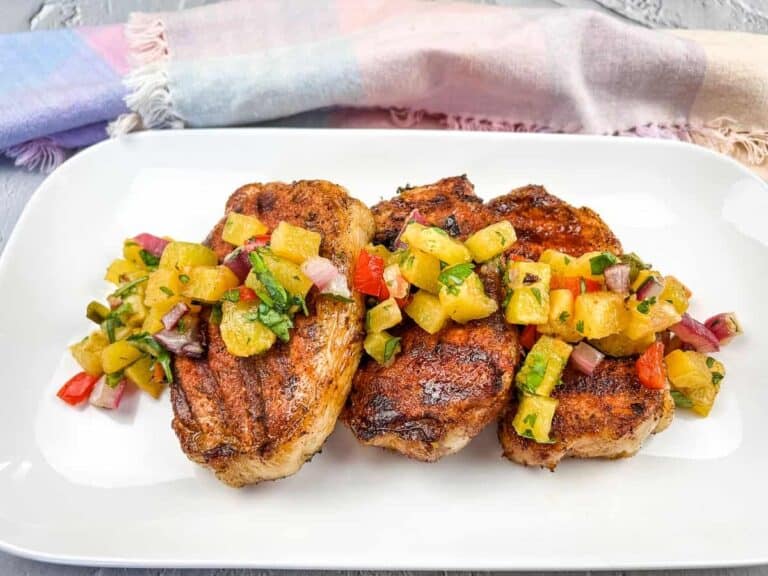 Grilled pork chops topped with pineapple salsa on a white plate, with a pastel-striped cloth in the background.