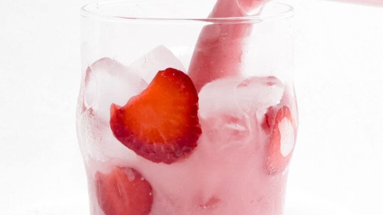 A clear glass filled with ice and sliced strawberries, with condensation visible on the exterior.