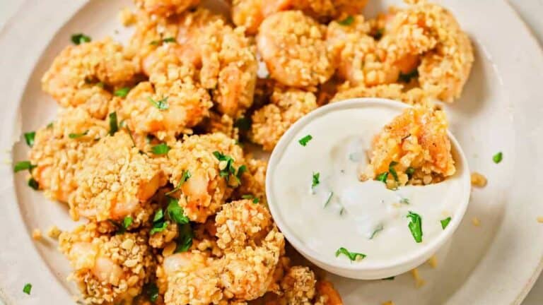 A plate of crispy, breaded shrimp garnished with chopped herbs, accompanied by a bowl of creamy dipping sauce.