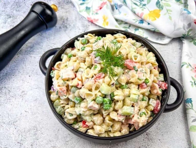 A bowl of salmon pasta salad with a creamy dressing, garnished with a sprig of dill.