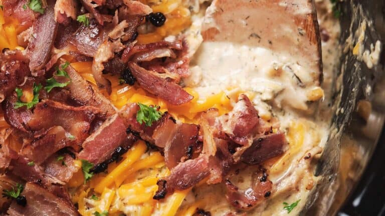 Cheesy chicken topped with crispy bacon and sprinkled with parsley in a black dish.