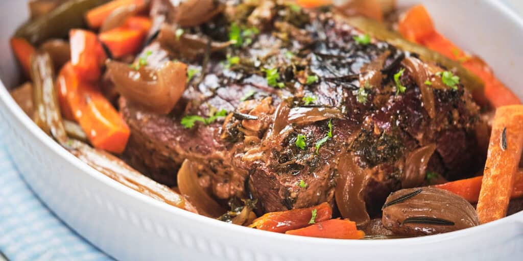 Pot roast with carrots and onions in a white dish, garnished with herbs.