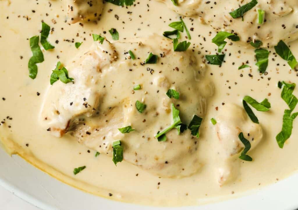 Creamy chicken dish garnished with chopped parsley and black pepper.