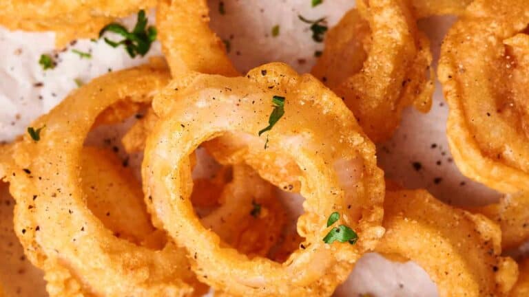 A close-up view of golden-brown, crispy fried onion rings garnished with chopped parsley and black pepper.