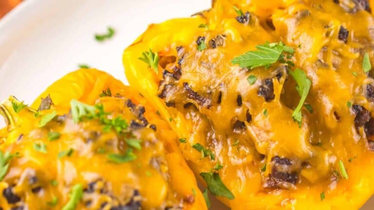 Close-up of stuffed bell peppers topped with melted cheese and garnished with fresh herbs on a white plate.