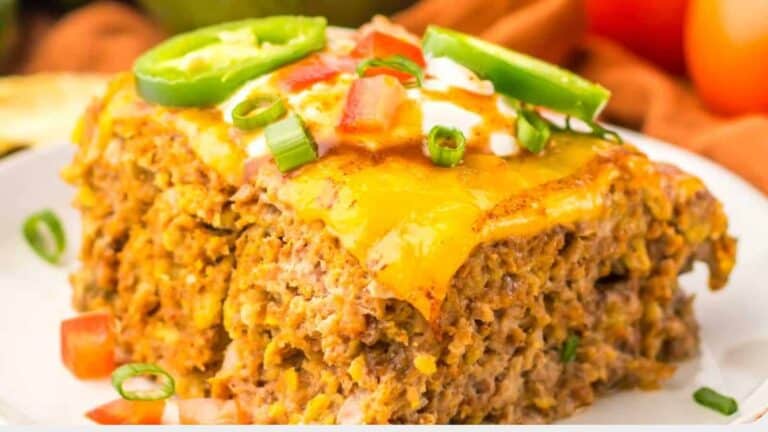 A close-up of a casserole slice topped with melted cheese, chopped tomatoes, green onions, and jalapeno slices on a plate.