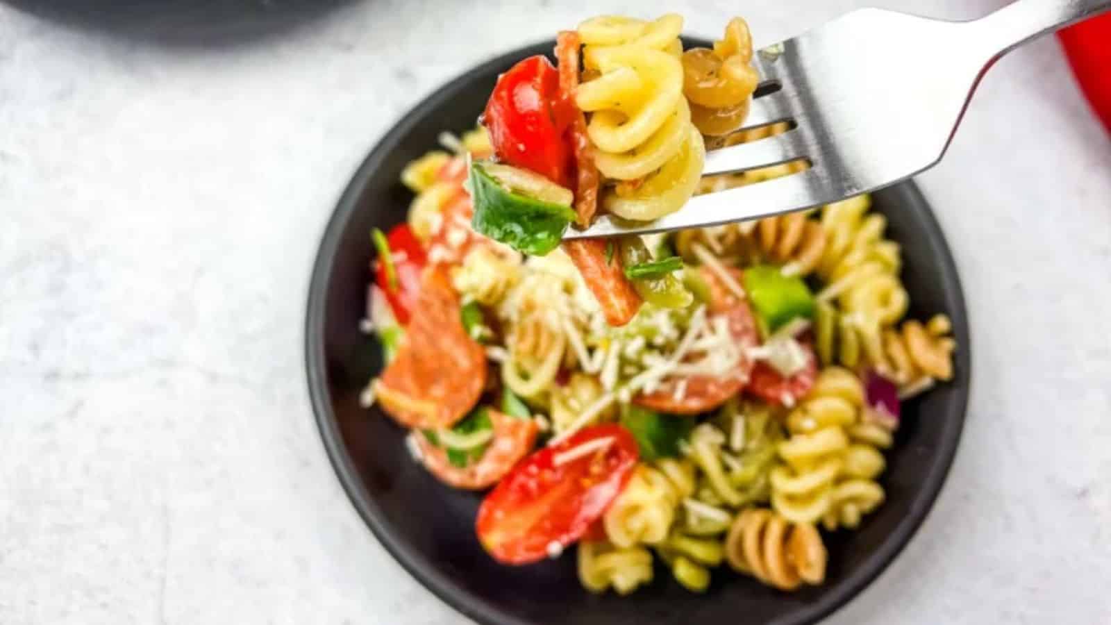 A fork with pizza pasta salad in a bowl.
