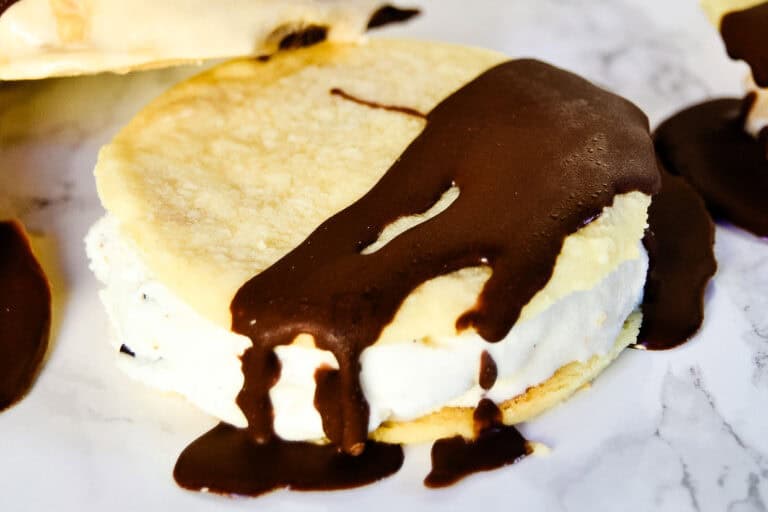 An ice cream sandwich with a chocolate coating partially covering the top and dripping down the sides, placed on a marble surface.