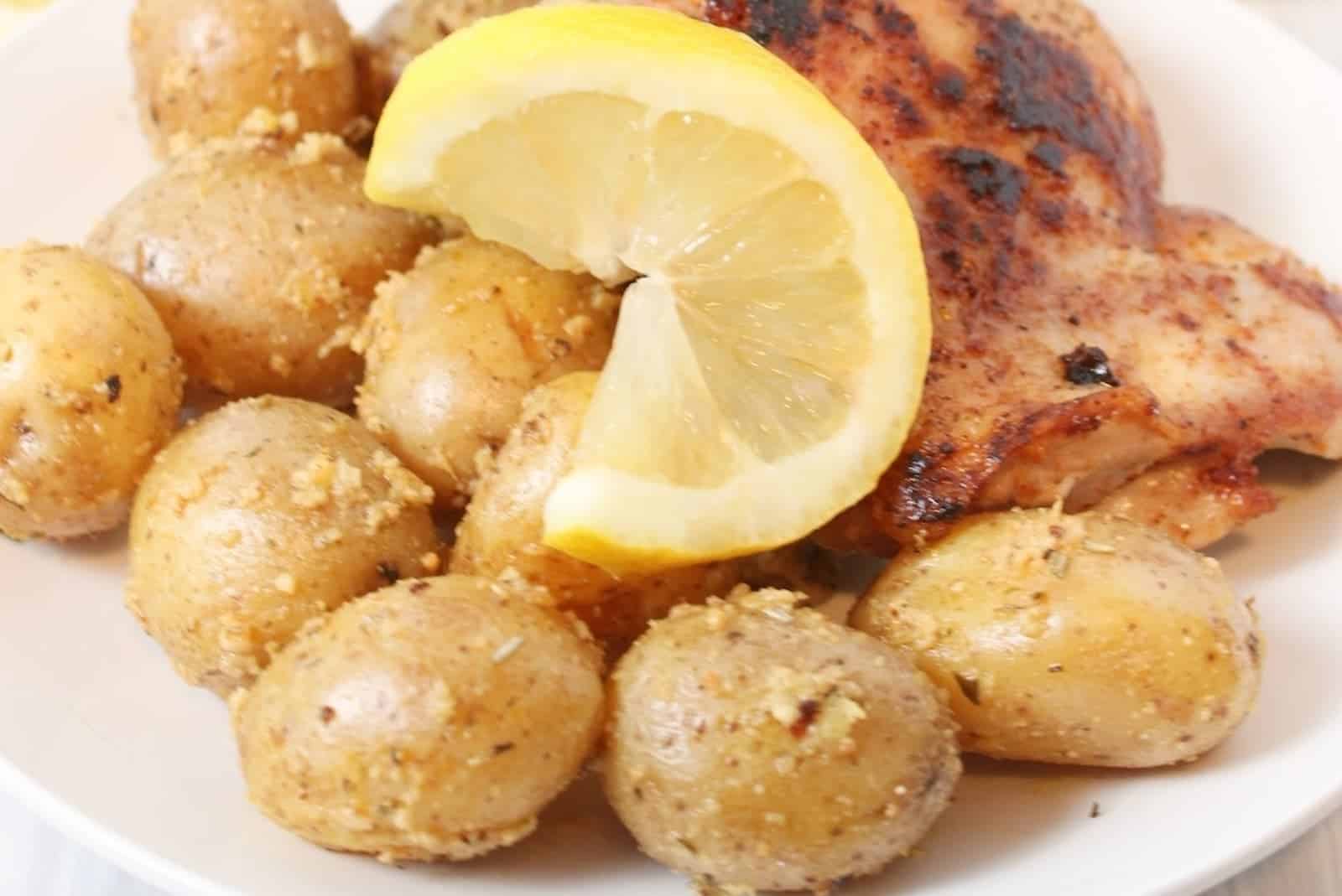 A plate with roasted chicken, seasoned baby potatoes, and a lemon wedge.