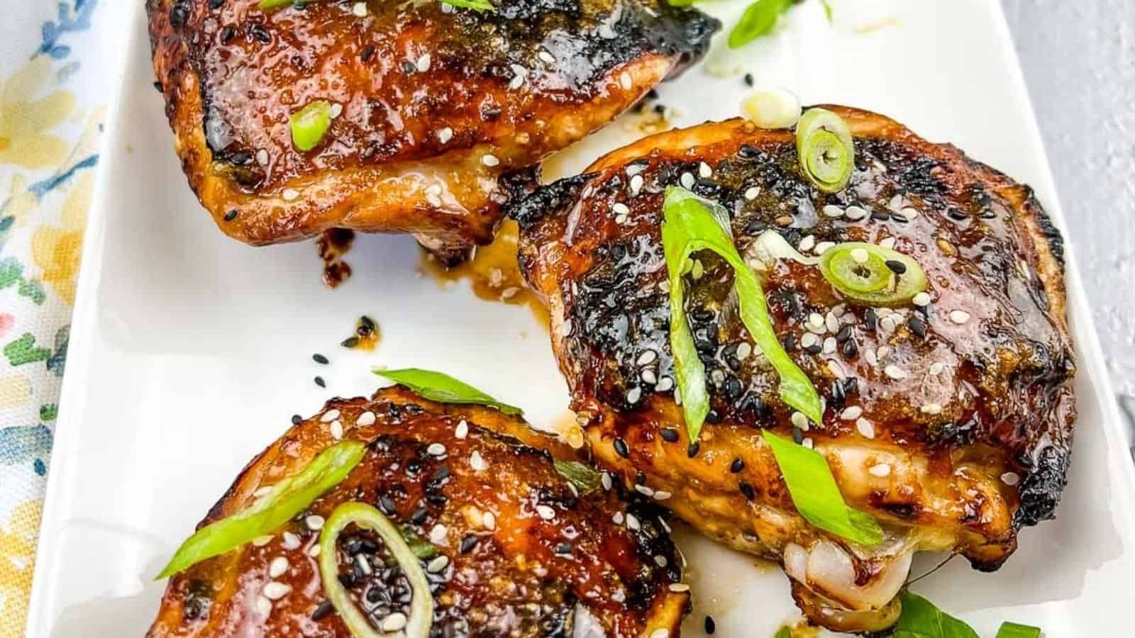 Three pieces of Air Fryer Honey Garlic Chicken garnished with sesame seeds and chopped green onions on a white rectangular plate.
