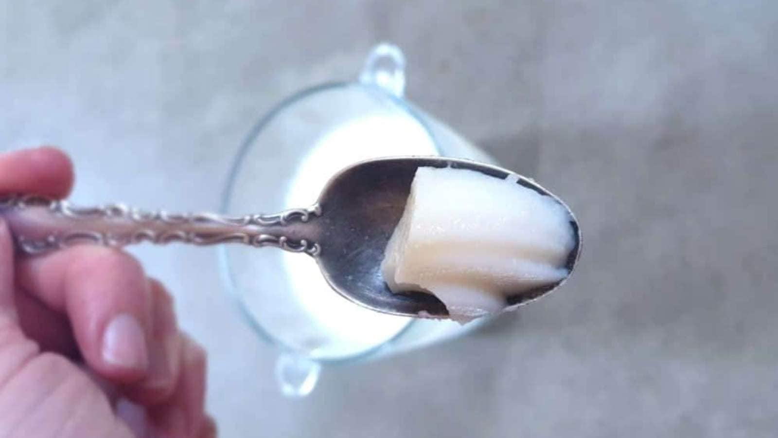 A hand holds a spoon with a bite of cheesecake pudding above a glass bowl.