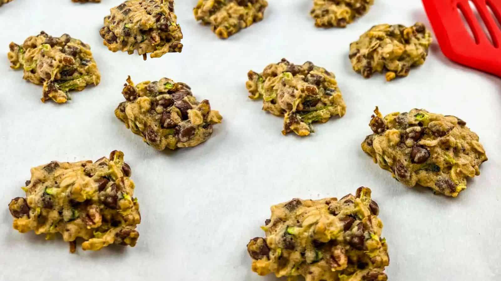 A batch of Zucchini cookies with chocolate & pecan on a parchment-lined baking sheet.