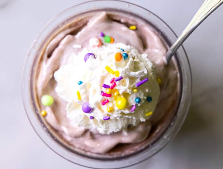 A dessert cup filled with chocolate mousse topped with whipped cream and colorful sprinkles, with a spoon in it.