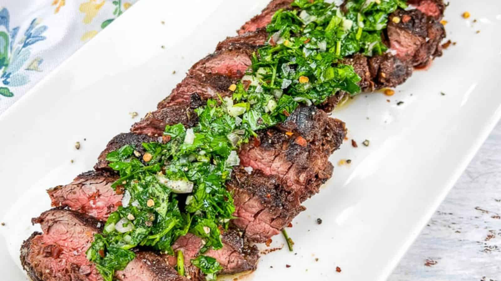 A plate of sliced grilled steak topped with a green herb sauce, served on a white rectangular dish.