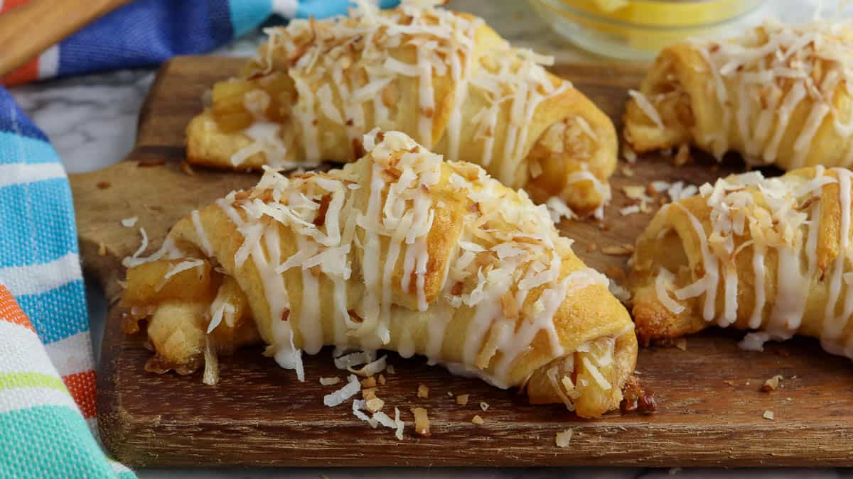 Freshly baked pineapple pastries topped with glaze and shredded coconut on a wooden board.