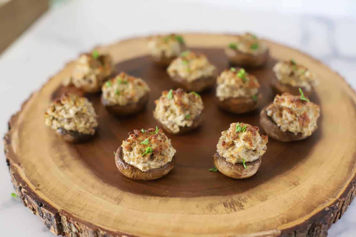 Stuffed mushrooms topped with herbs arranged on a wooden platter.