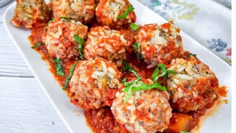 A white rectangular plate features meatballs topped with grated cheese and garnished with chopped herbs, resting on a bed of tomato sauce.