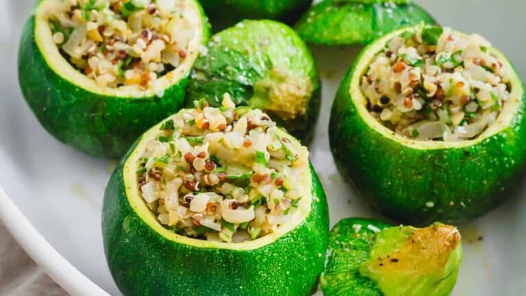 Round zucchini stuffed with a mixture of rice, quinoa, and herbs, with their tops placed next to them on a white plate.