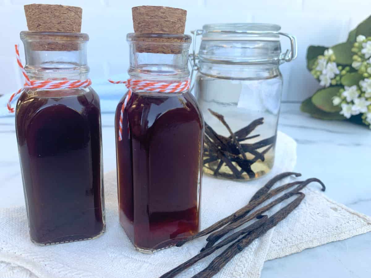 Two glass bottles filled with dark vanilla extract and several loose vanilla beans.