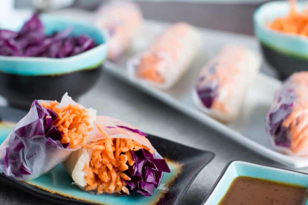 Plates of vegetable spring rolls with purple cabbage and shredded carrots, served with dipping sauce.